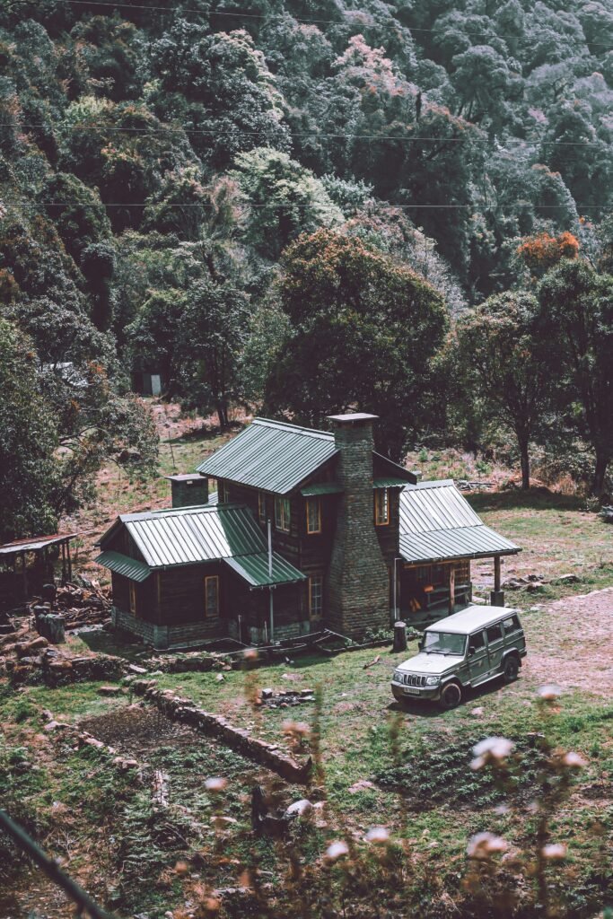 A wooden cottage and parked vehicle beneath wooded slopes in Dzuleke