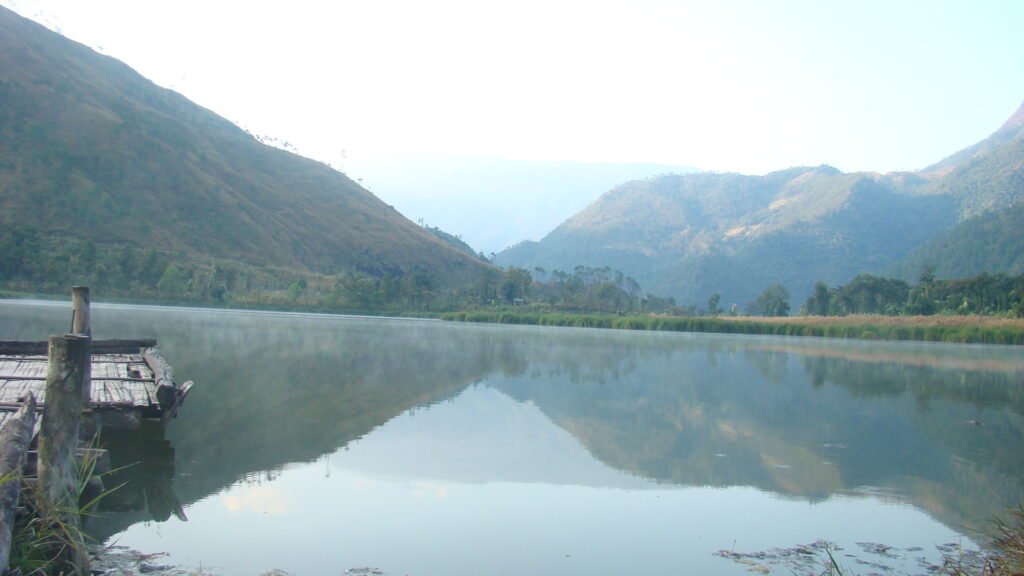 Shilloi Lake reflecting forested hills, with a wooden jetty